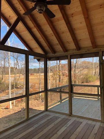 Screened porch with wooden ceiling, deck, and view of trees and fields.