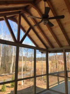 Screened porch with wooden frame, ceiling fan, and view of trees and landscape.