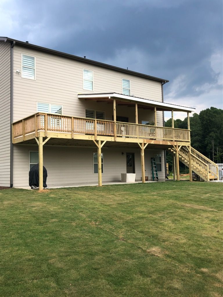 Two-story house with a wooden deck and stairs; green lawn under a cloudy sky.