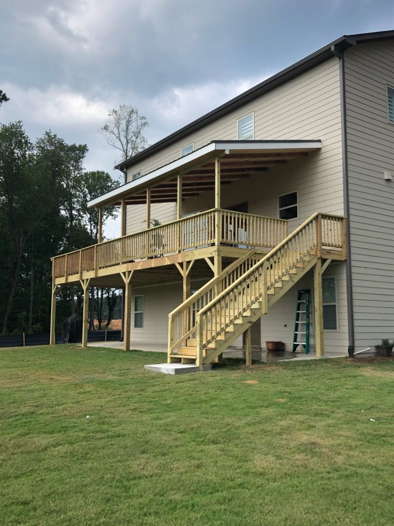 Wooden deck attached to a two-story beige house with stairs. Green grass and overcast sky.