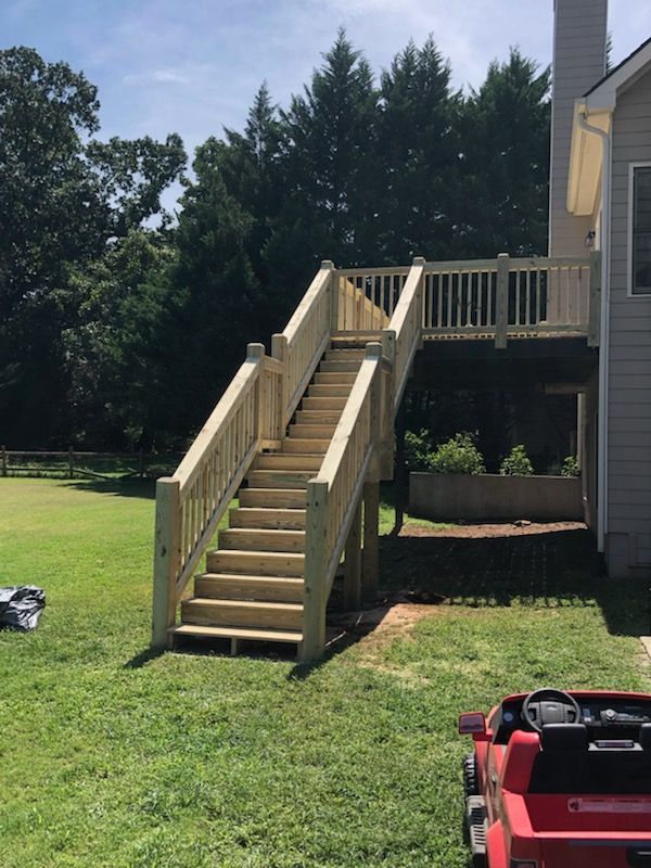 Wooden staircase leading up to an elevated deck attached to a gray house, set in a grassy yard.