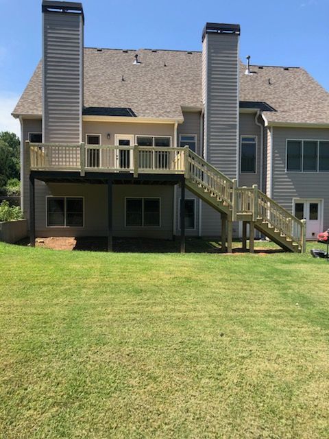 Back view of a light gray house with a wooden deck and stairs, with two chimneys, on a green lawn.