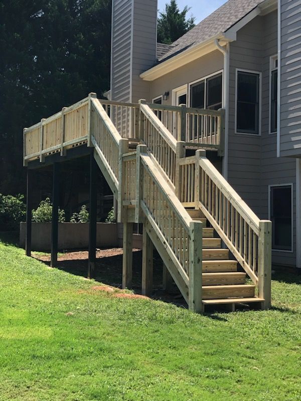 Wooden deck and stairs attached to a house with gray siding, set on a green lawn.
