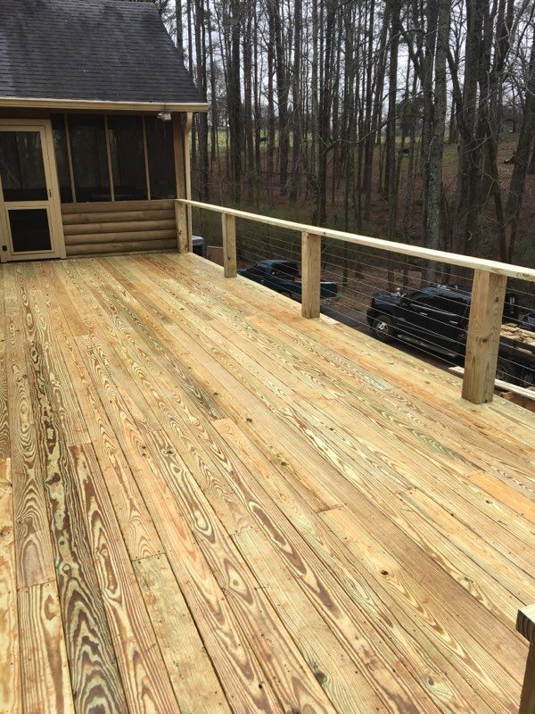 Wooden deck with a screened porch and wooded background.