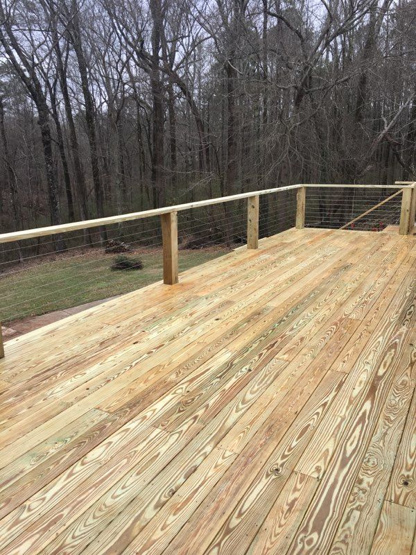 Wooden deck with metal cable railing, overlooking a yard and trees.