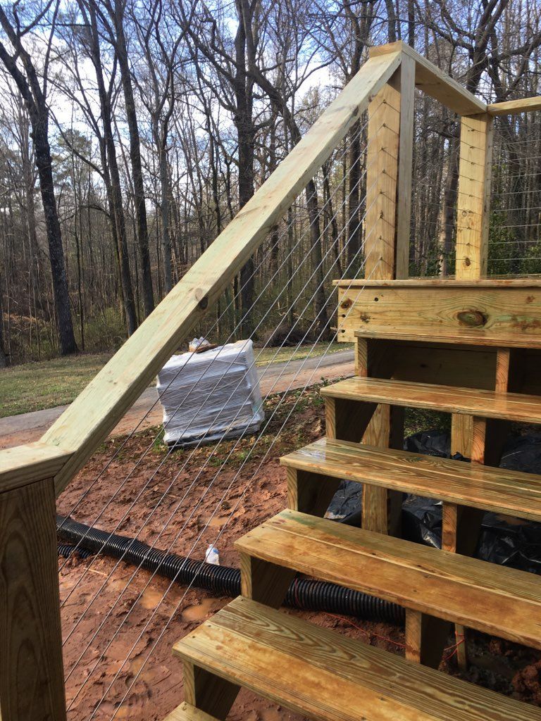 Wooden deck stairs with wire mesh railing, built outdoors near trees and construction materials.