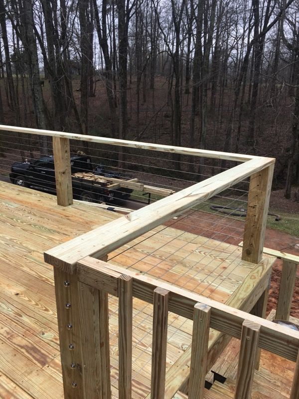 Wooden deck with cable railing overlooking a wooded area.