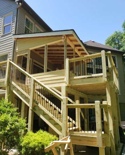 Wooden deck and screened porch attached to a multi-story house. Sunlight.