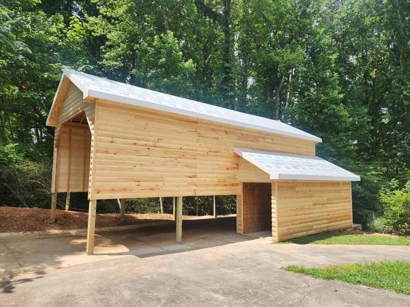 Wooden carport with a white roof and supports over a concrete driveway, surrounded by trees.