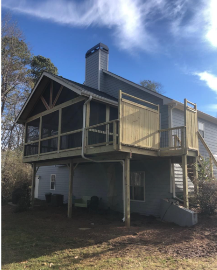 Two-story house with a screened porch and deck, painted blue. Bright blue sky overhead.