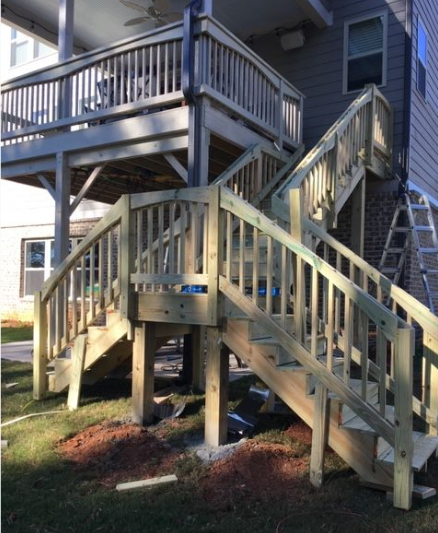 Wooden deck with stairs leading down to grass, attached to a house with siding.