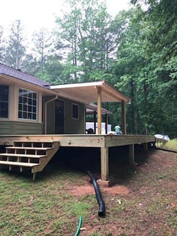 Wooden deck with stairs attached to a house with a covered porch.