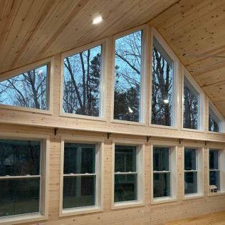 A wooden room with a large, multi-pane window wall showing trees outside and a slanted ceiling with recessed lighting.