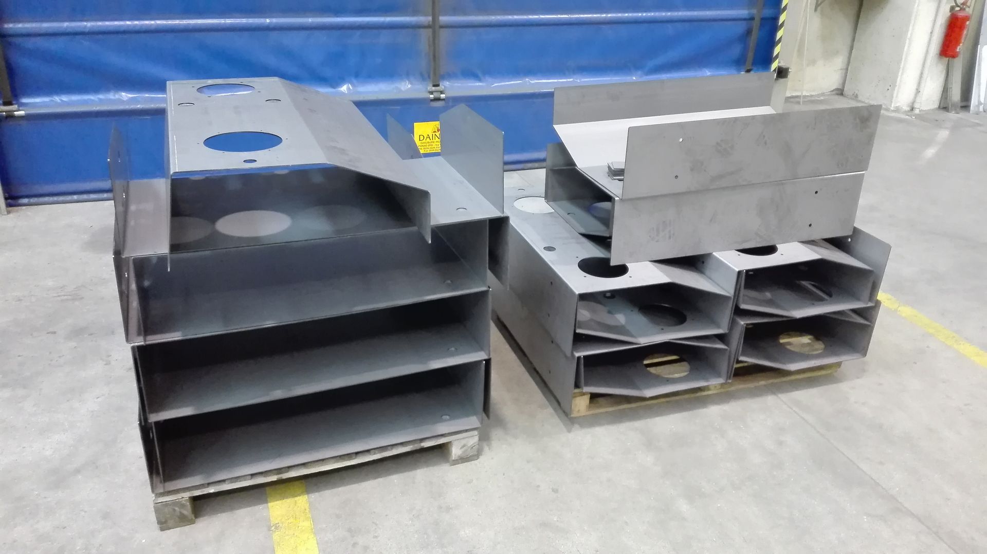 Componenti industriali in metallo nero e grigio impilati su pallet in un'area di magazzino.