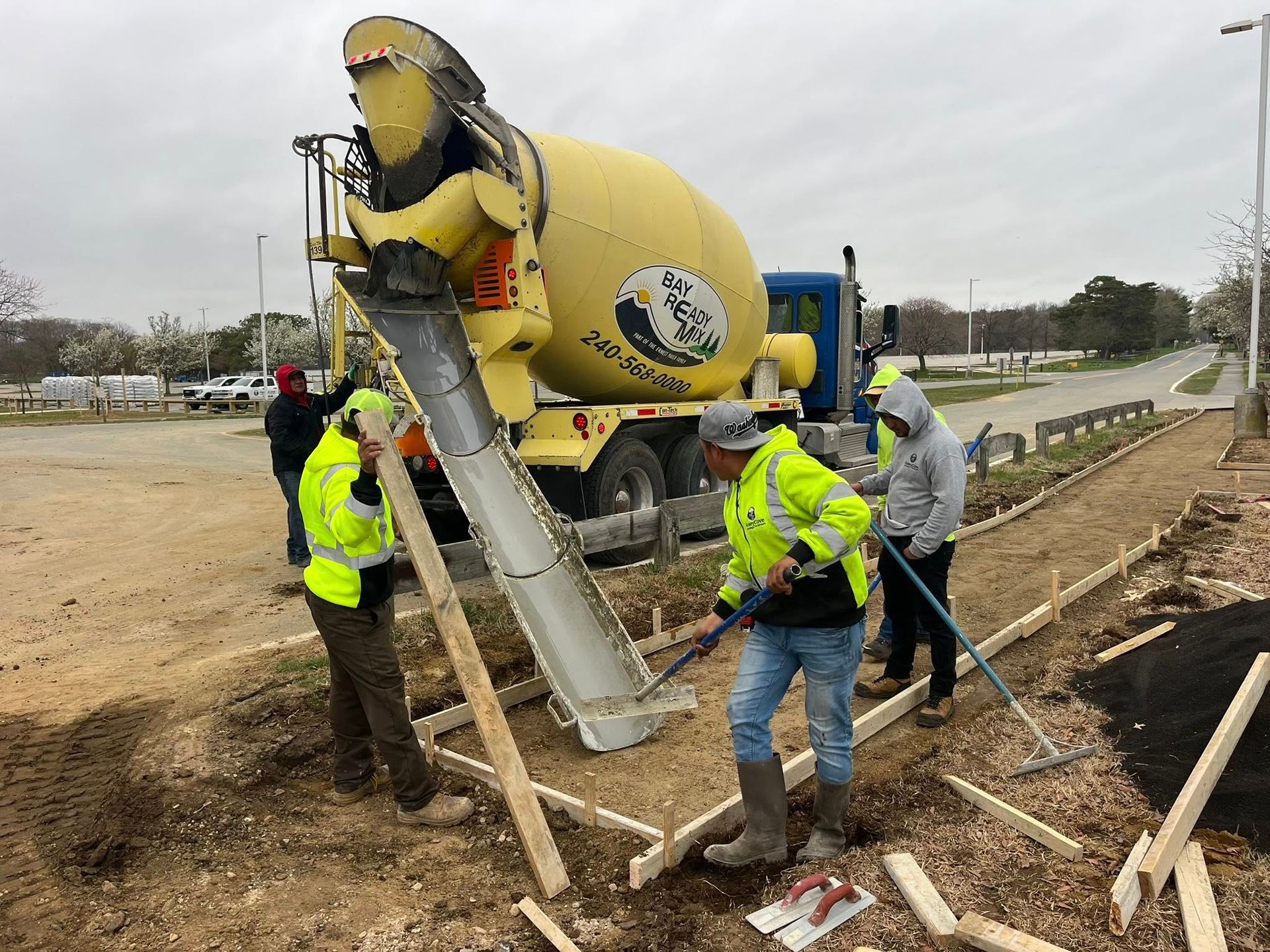 Workers in neon vests guide a cement truck chute at a road construction site.
