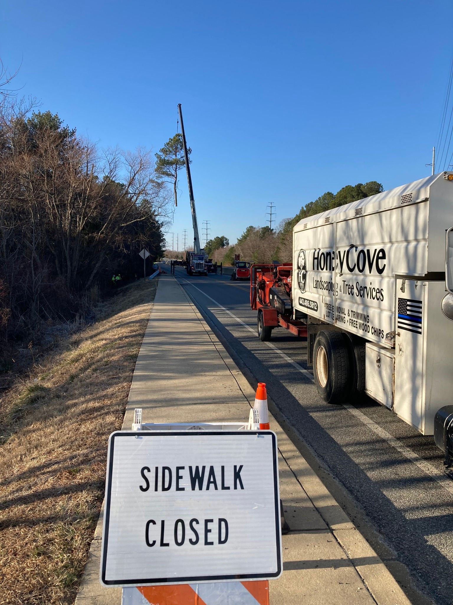 Sidewalk closed sign beside a road work truck blocking a paved path under a clear blue sky
