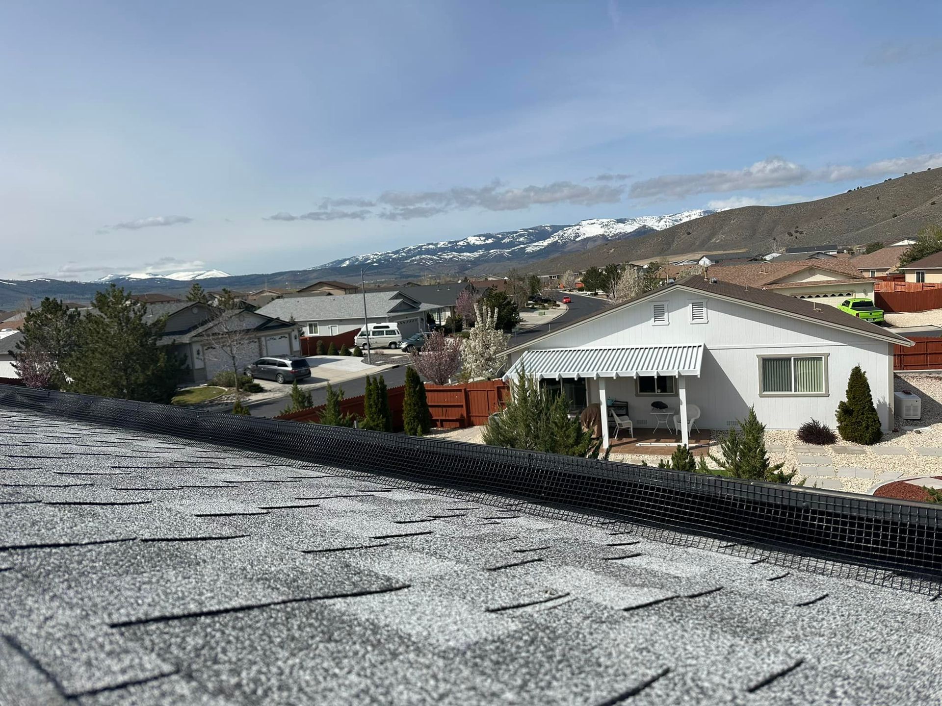 A rooftop view of a residential area with a house in the foreground and mountains in the background.