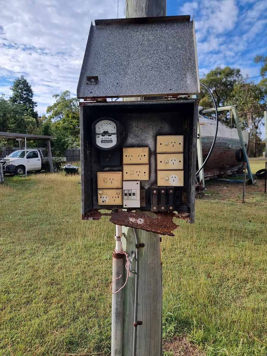 A Rusty Electrical Box Is Sitting On Top Of A Wooden Pole In A Field — AA Electrical Co in Yeppoon, QLD