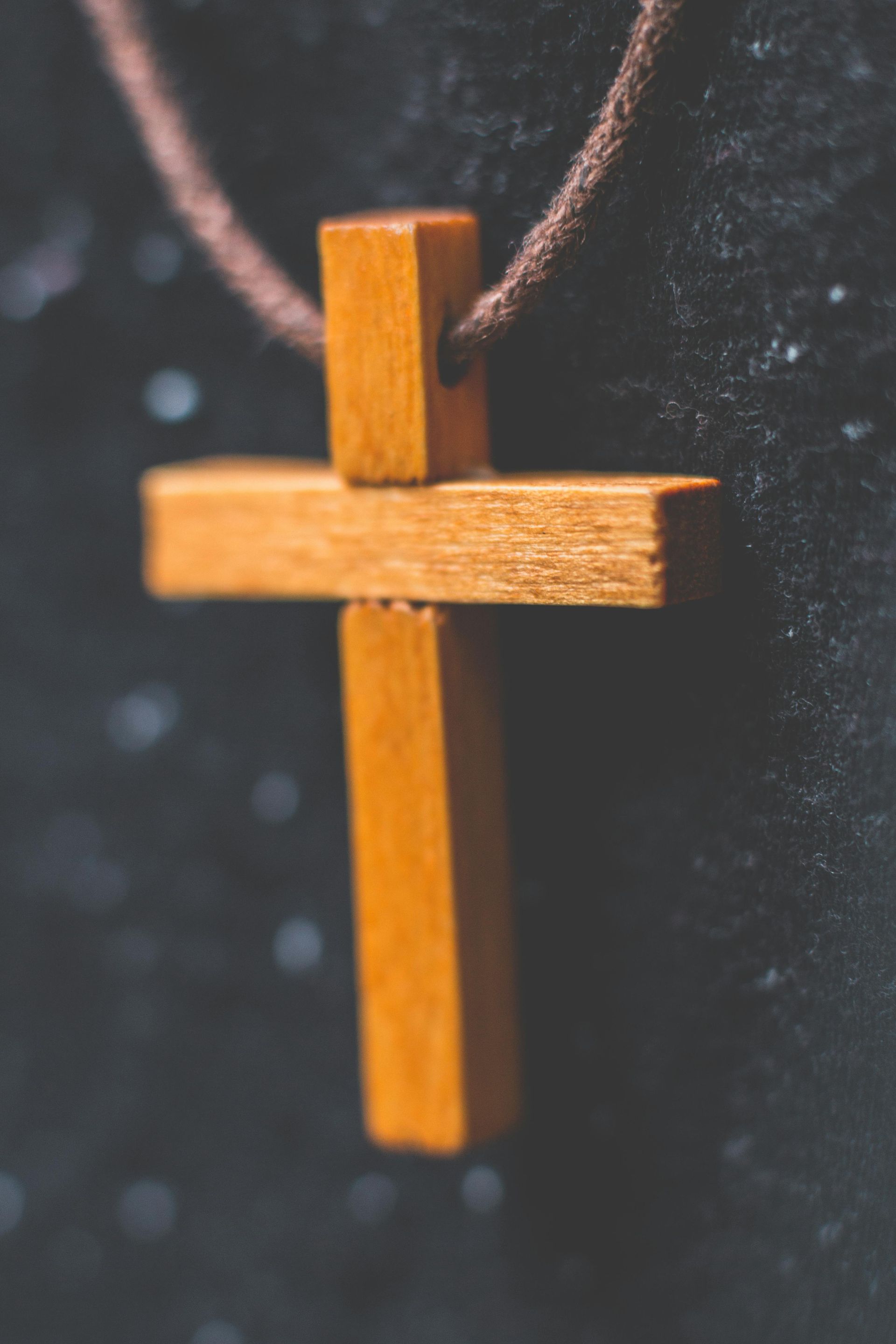 A wooden cross is hanging from a brown string on a black background.