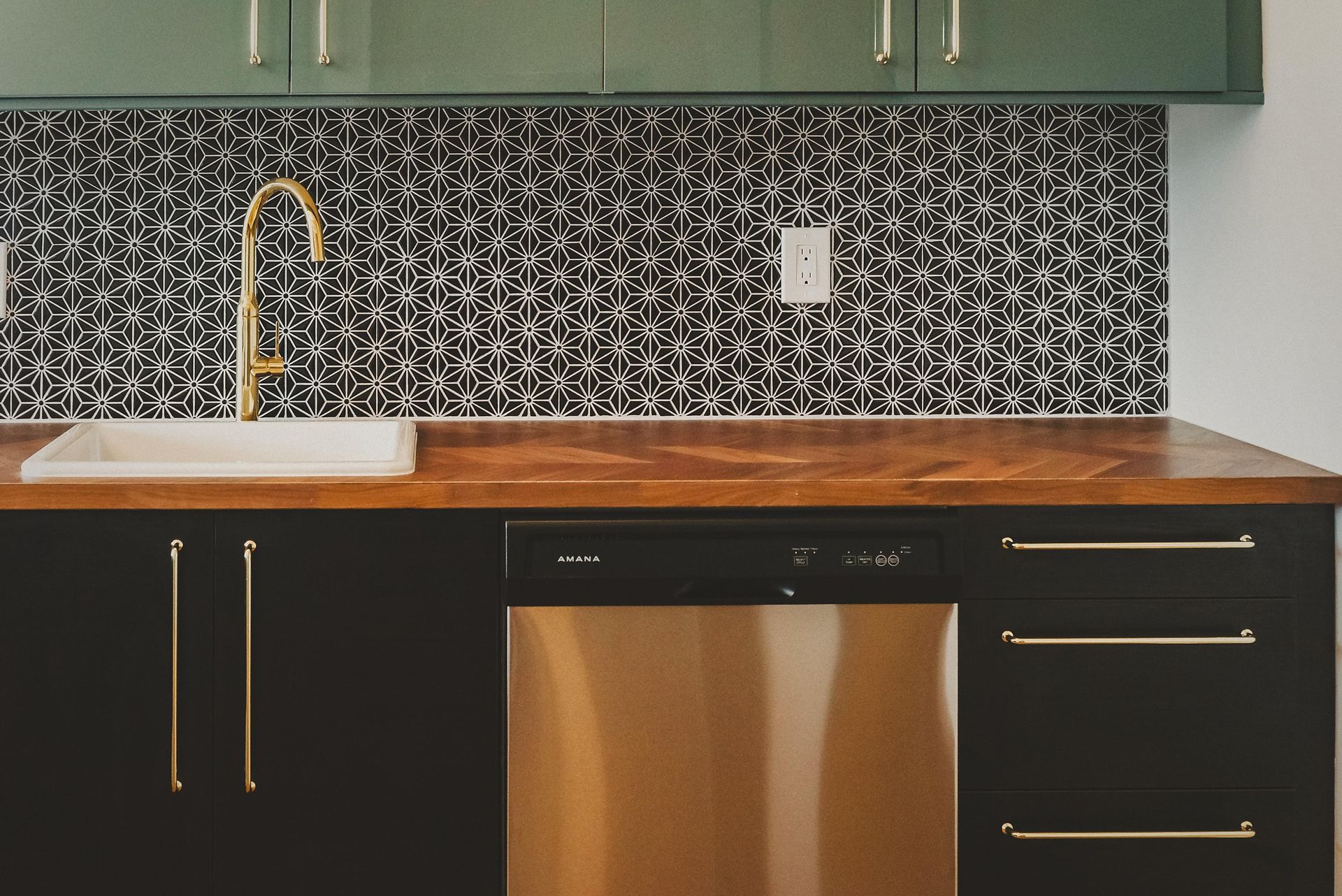 Kitchen with black cabinets, patterned tile backsplash, and gold faucet.