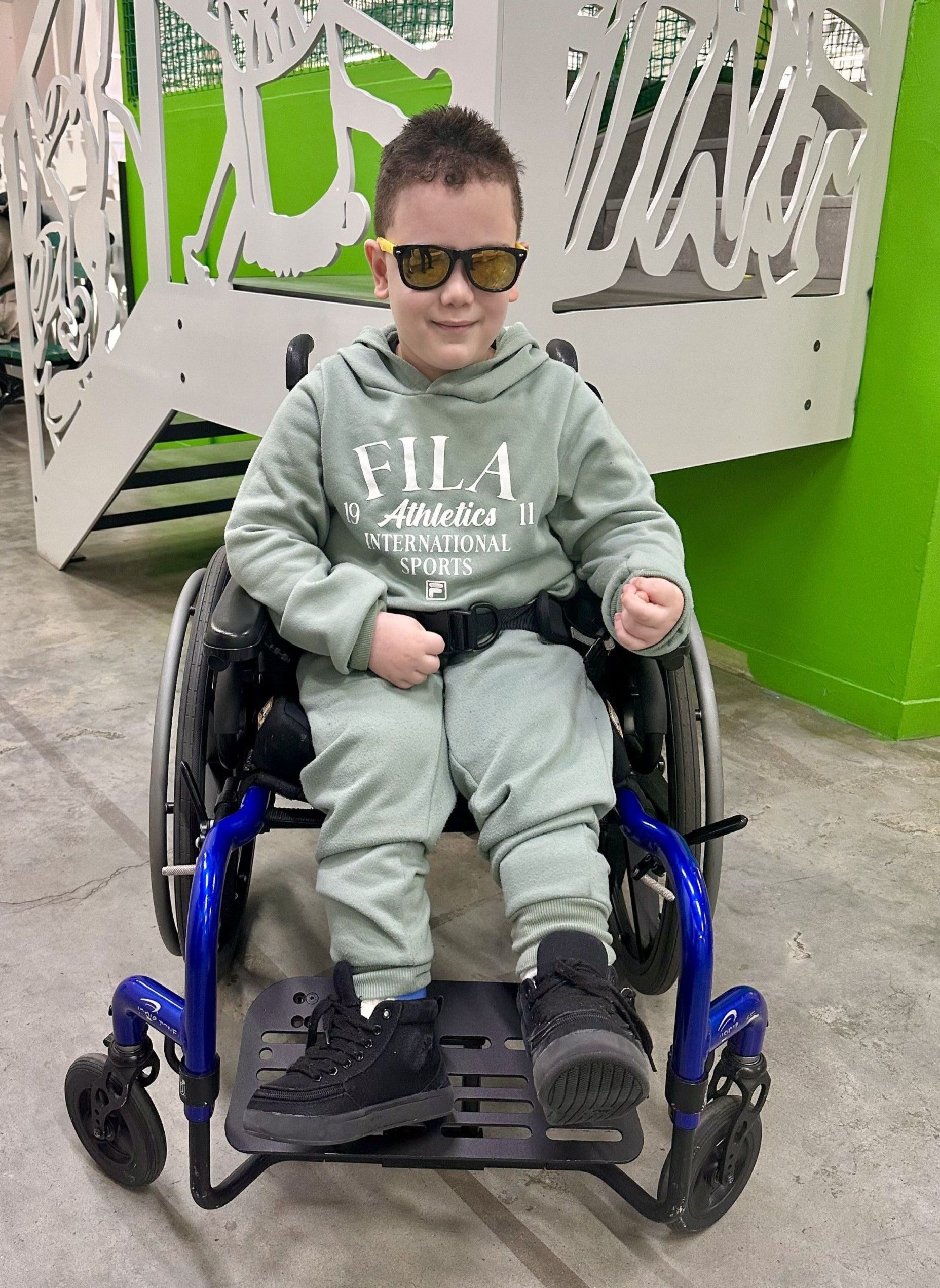 A young boy is sitting in a wheelchair wearing sunglasses.