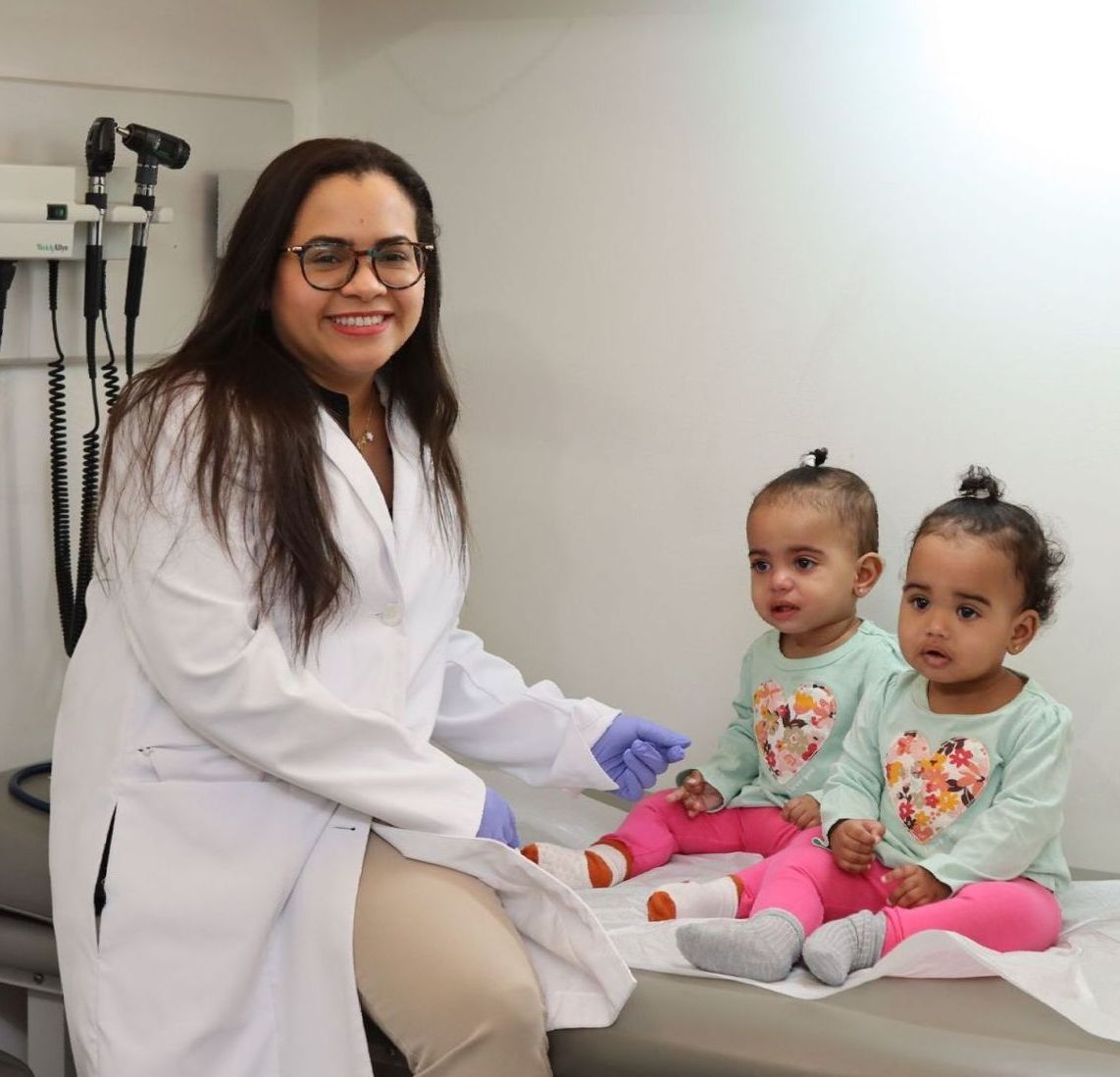 Female pediatrician with two small girls on a medical table. The doctor is smiling.