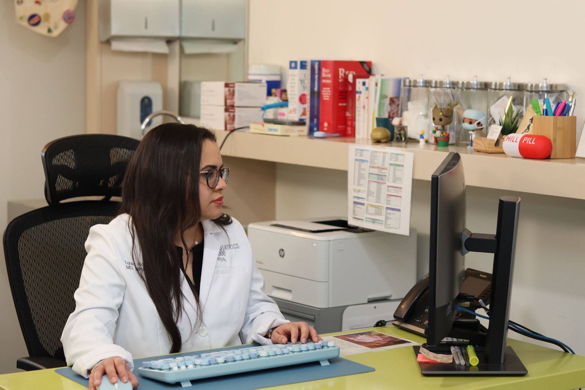 A woman in a lab coat is sitting at a desk using a computer.