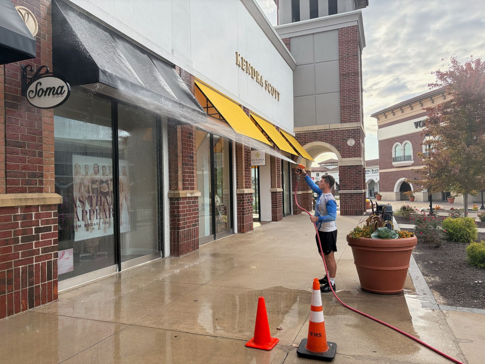 Person standing by orange cones outside a storefront on a rainy sidewalk