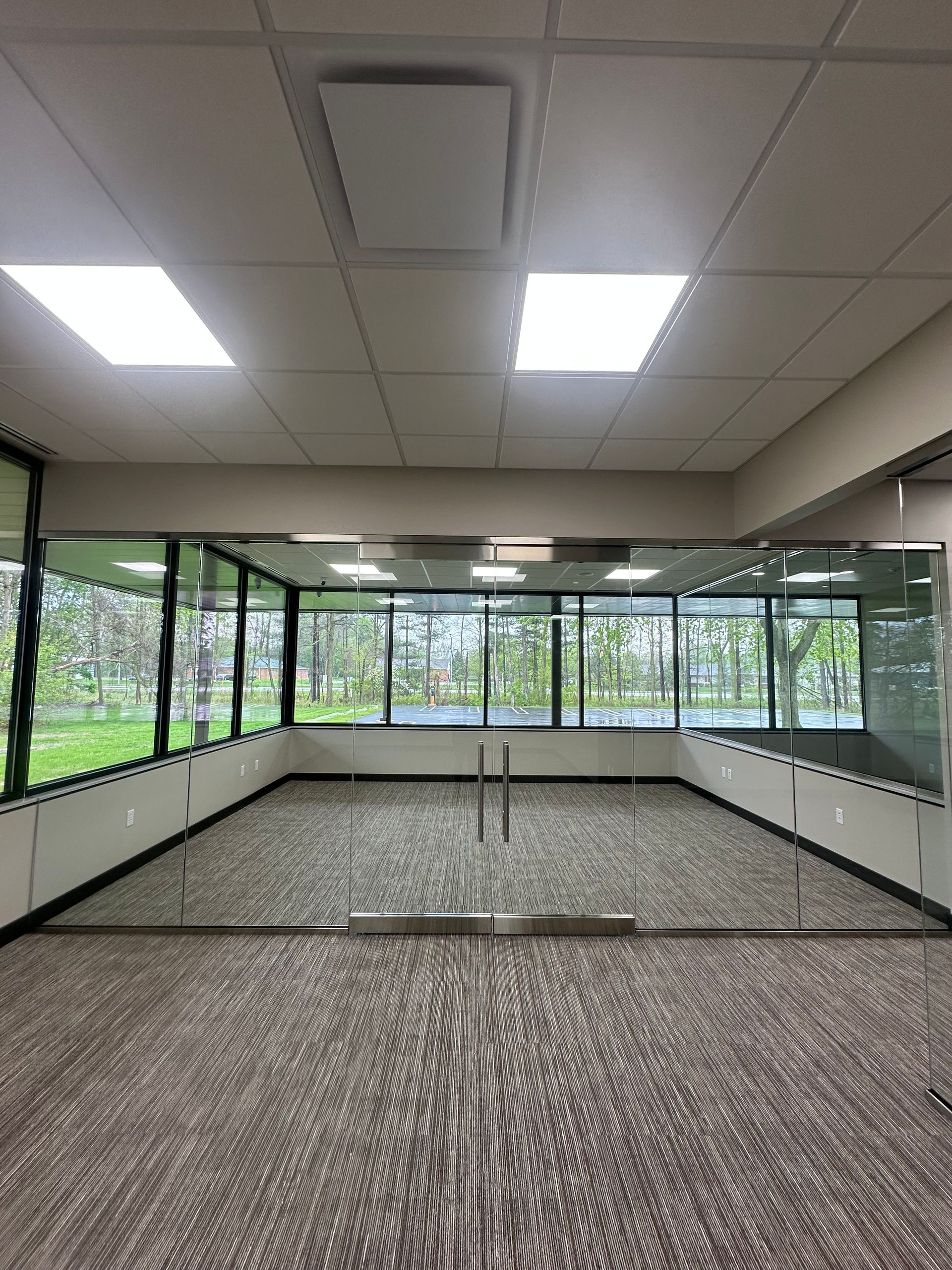 Empty carpeted office room with large windows and fluorescent ceiling lights