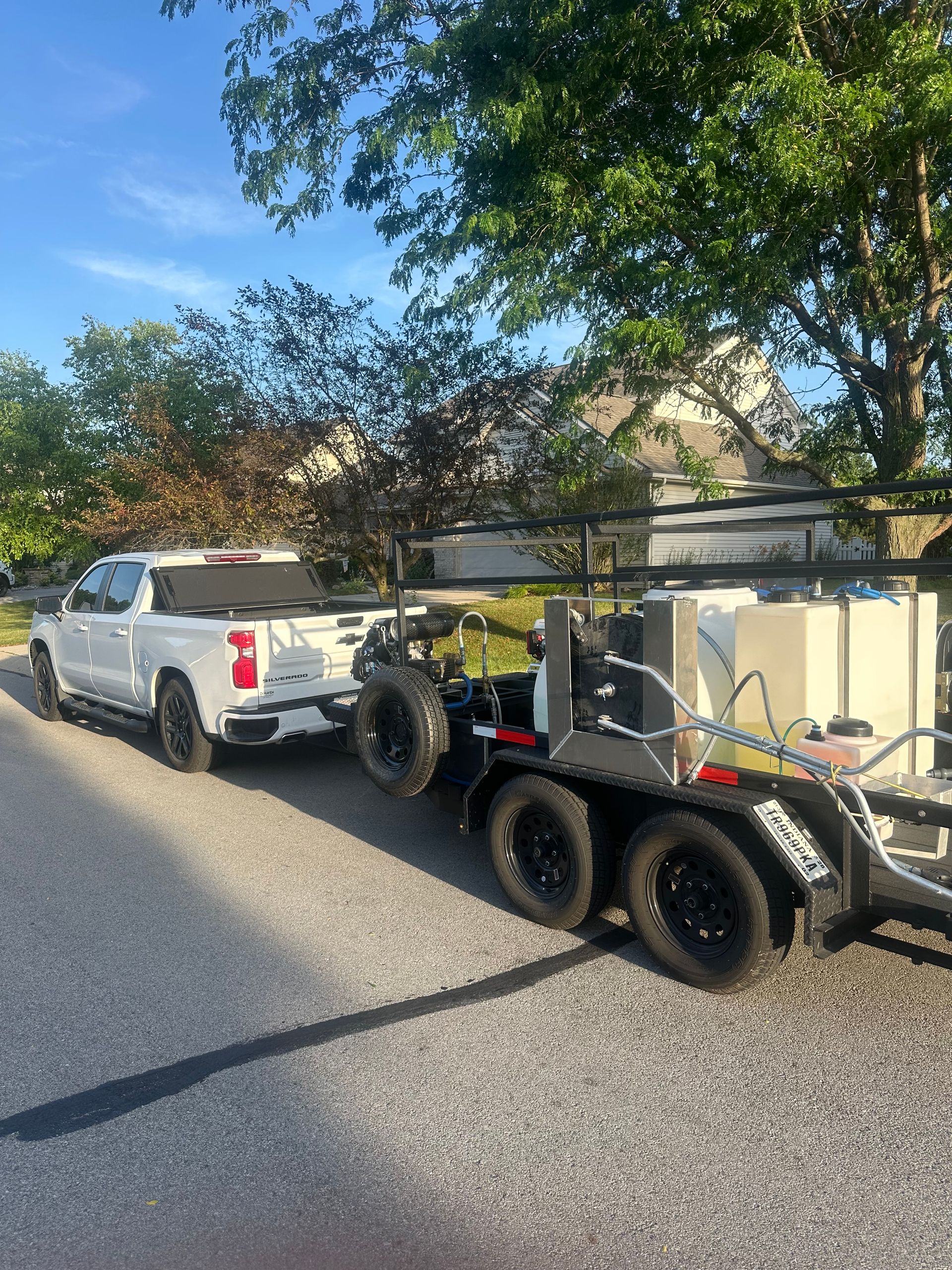 White pickup truck towing a black utility trailer on a sunny residential street.