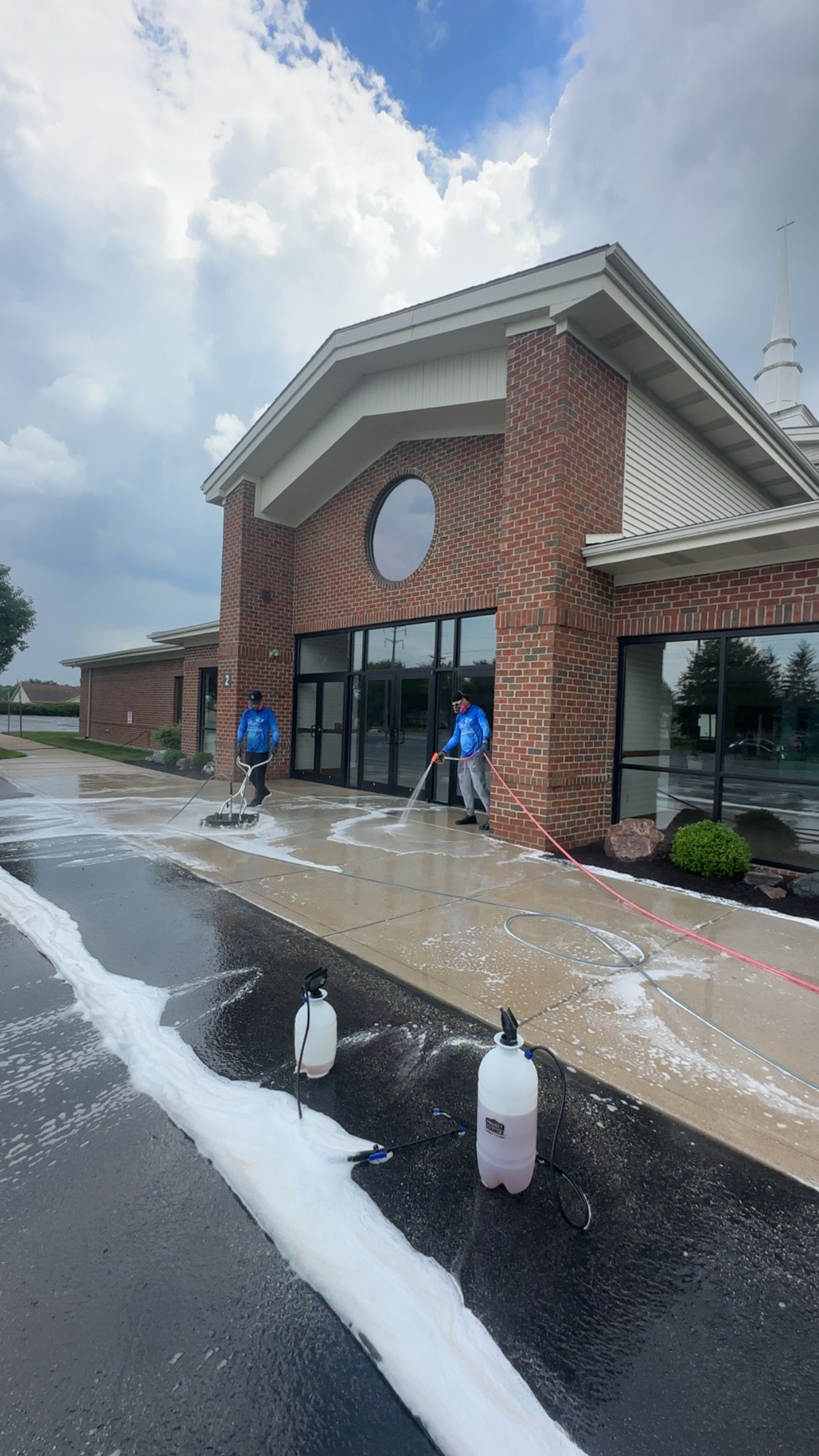 Brick storefront with people standing outside after water is sprayed across the wet pavement.