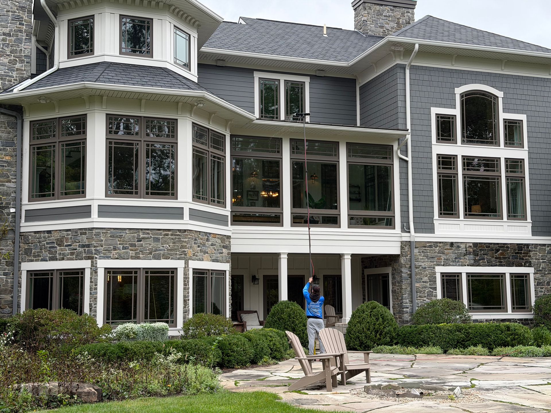 Large gray house with many windows, a stone patio, and outdoor chairs in front of the entrance
