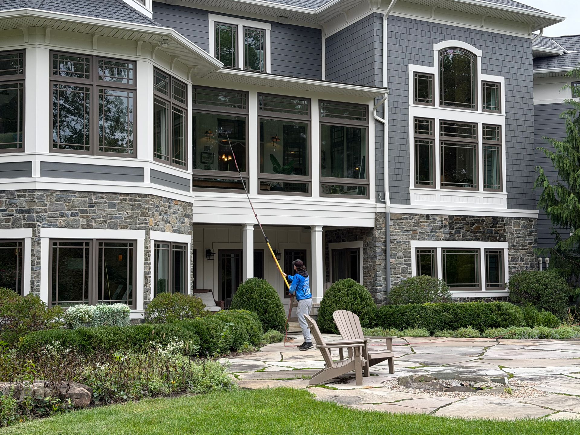 Large stone house with tall windows and a person cleaning the patio with a pressure washer