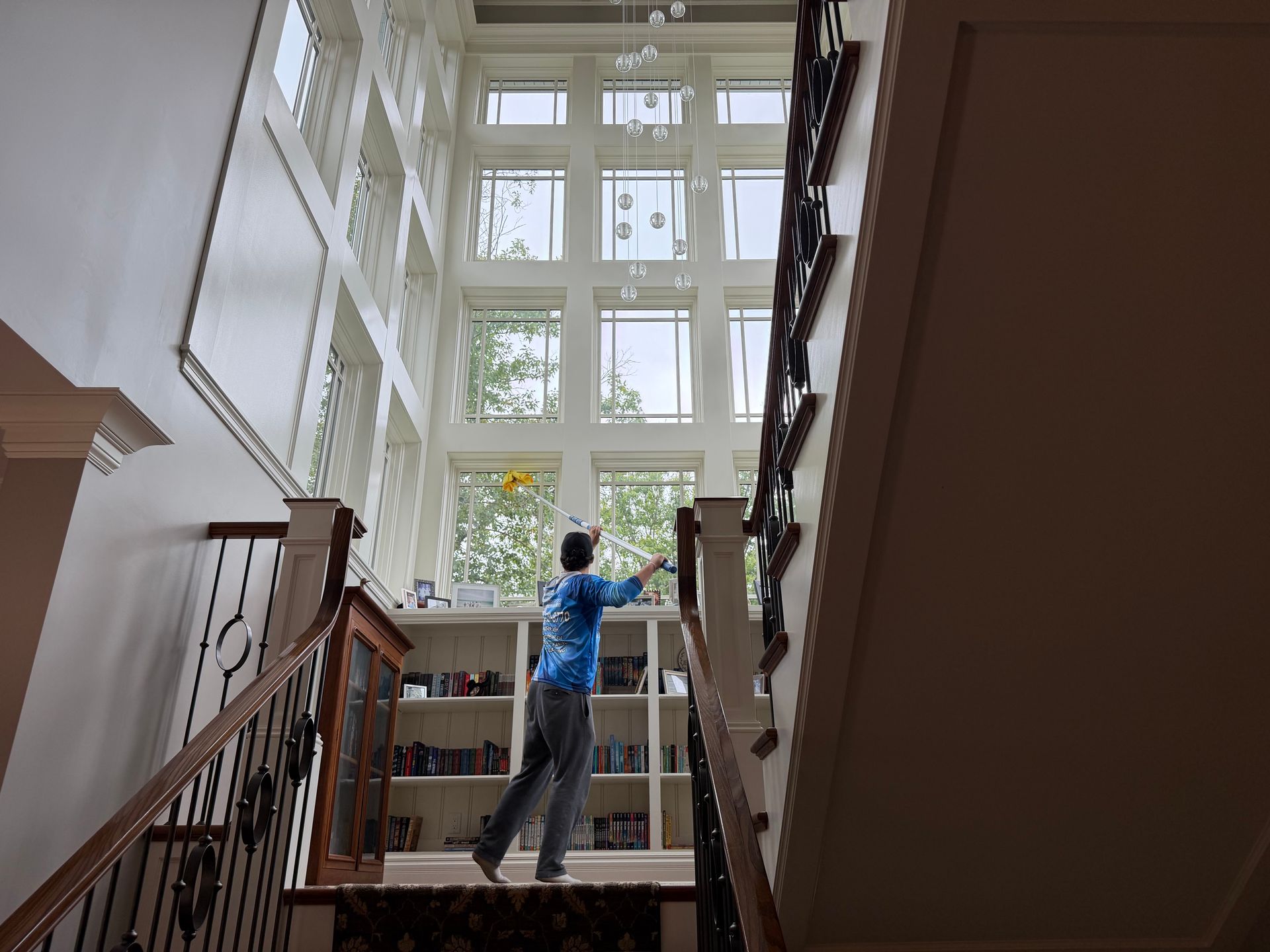 Person on staircase reaching toward large sunlit window in a home interior