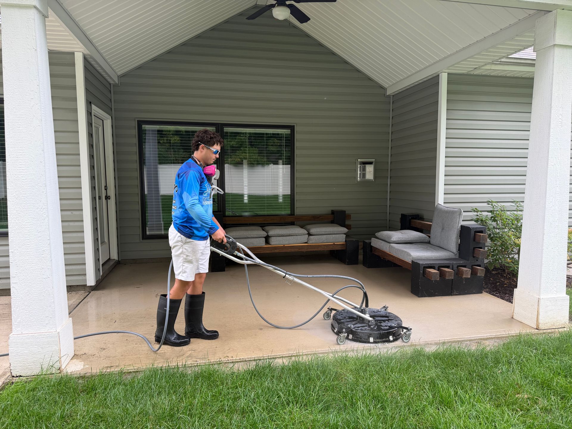 Person mowing grass with a push mower on a covered patio near outdoor furniture