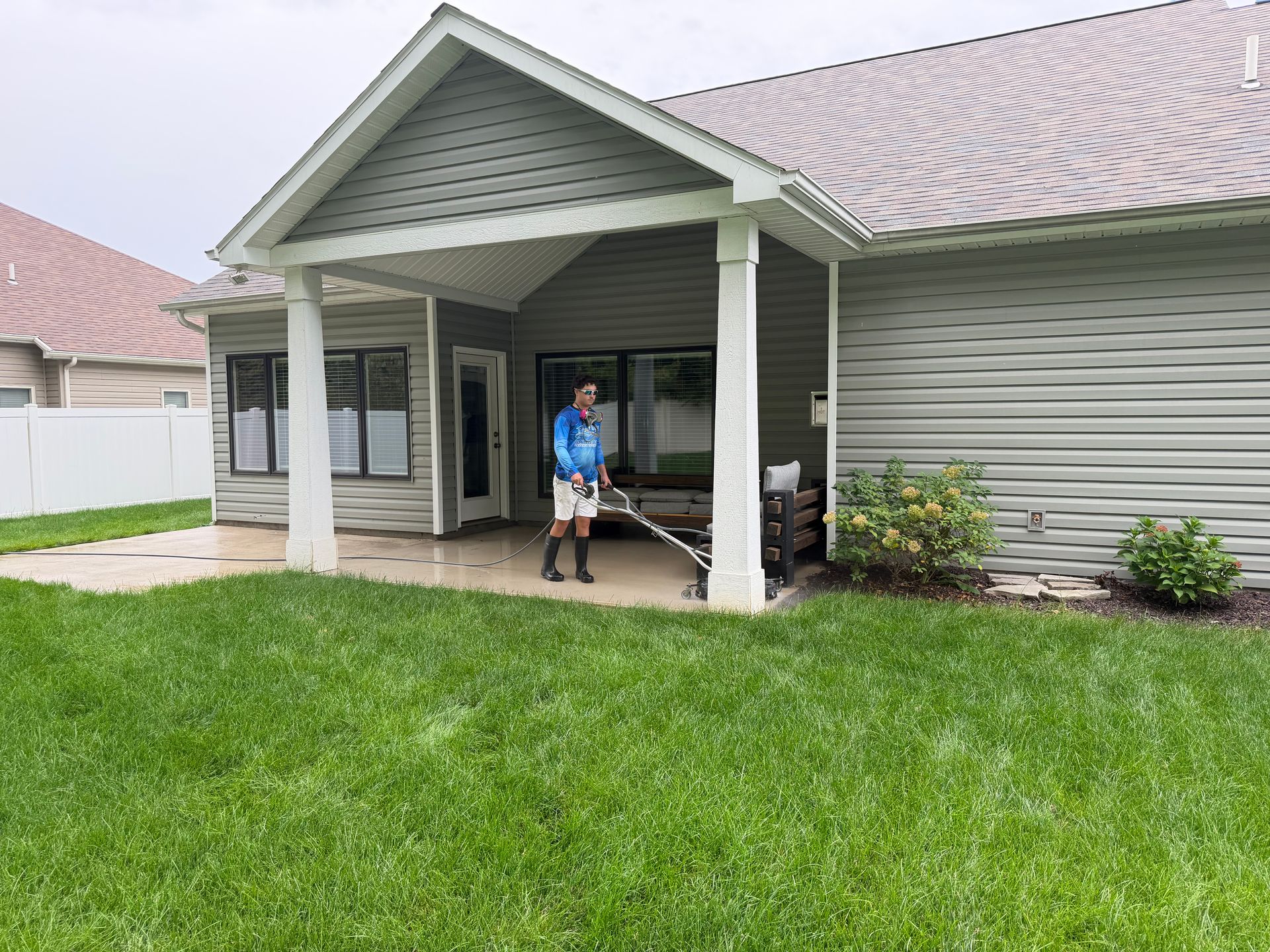 Person standing on a covered porch of a house with green lawn in front