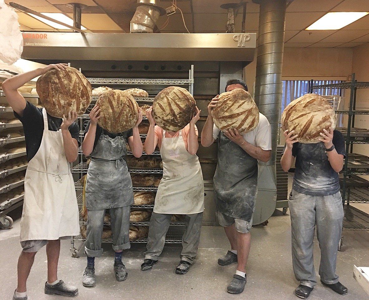 A group of people holding large loaves of bread in front of their faces