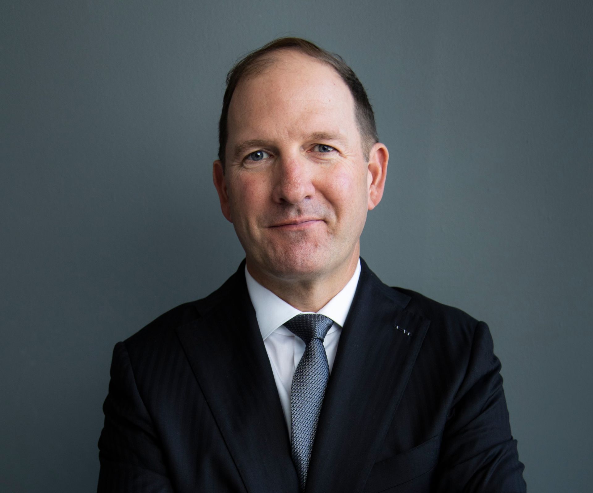 A man in a suit and tie is standing with his arms crossed.