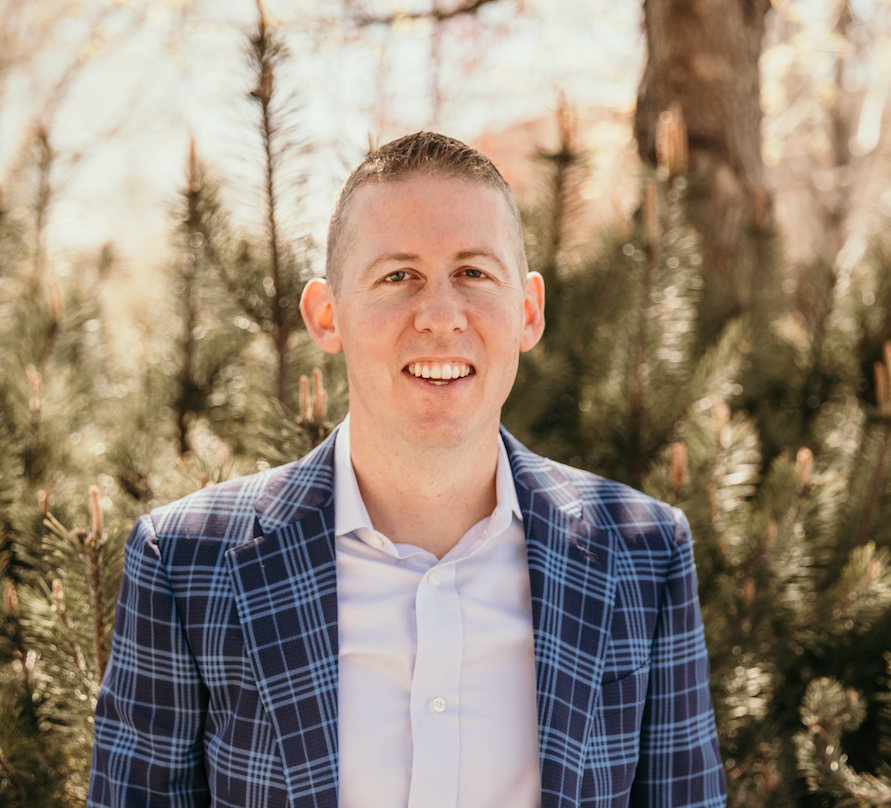 A man in a suit and white shirt is standing in front of a christmas tree.