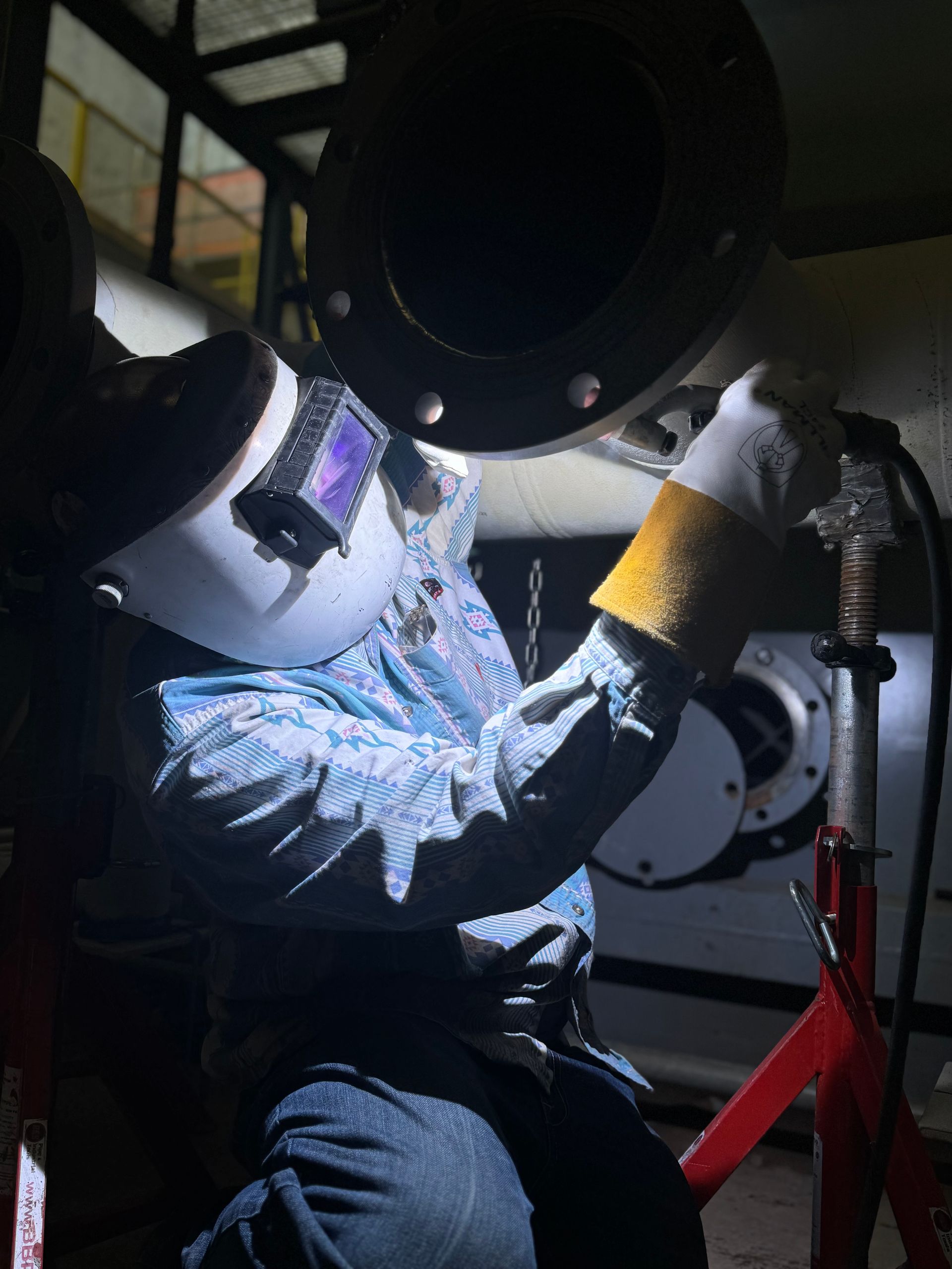 A man wearing a welding mask is welding a pipe in a dark room.