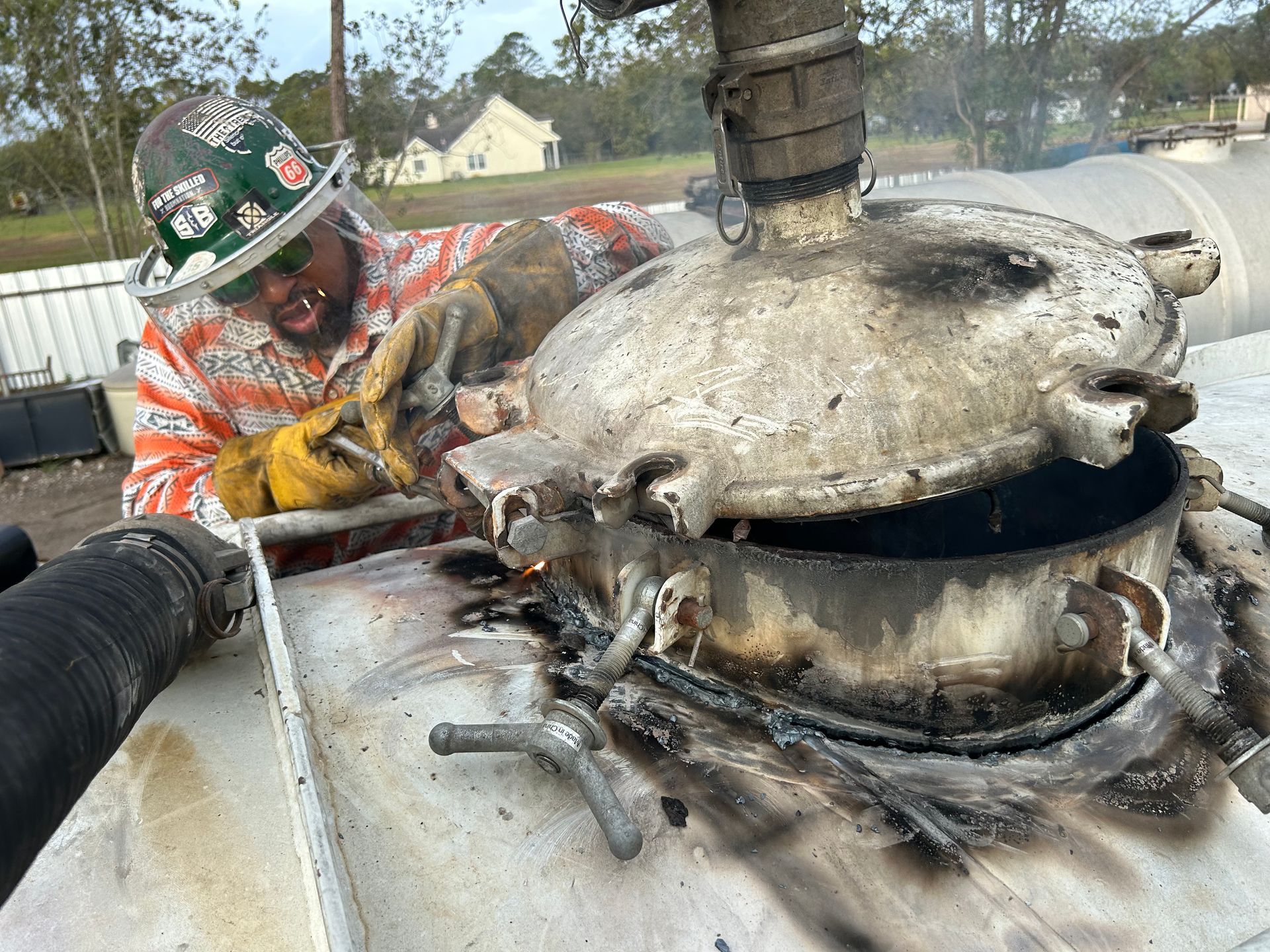 A man wearing a hard hat is working on a metal object.
