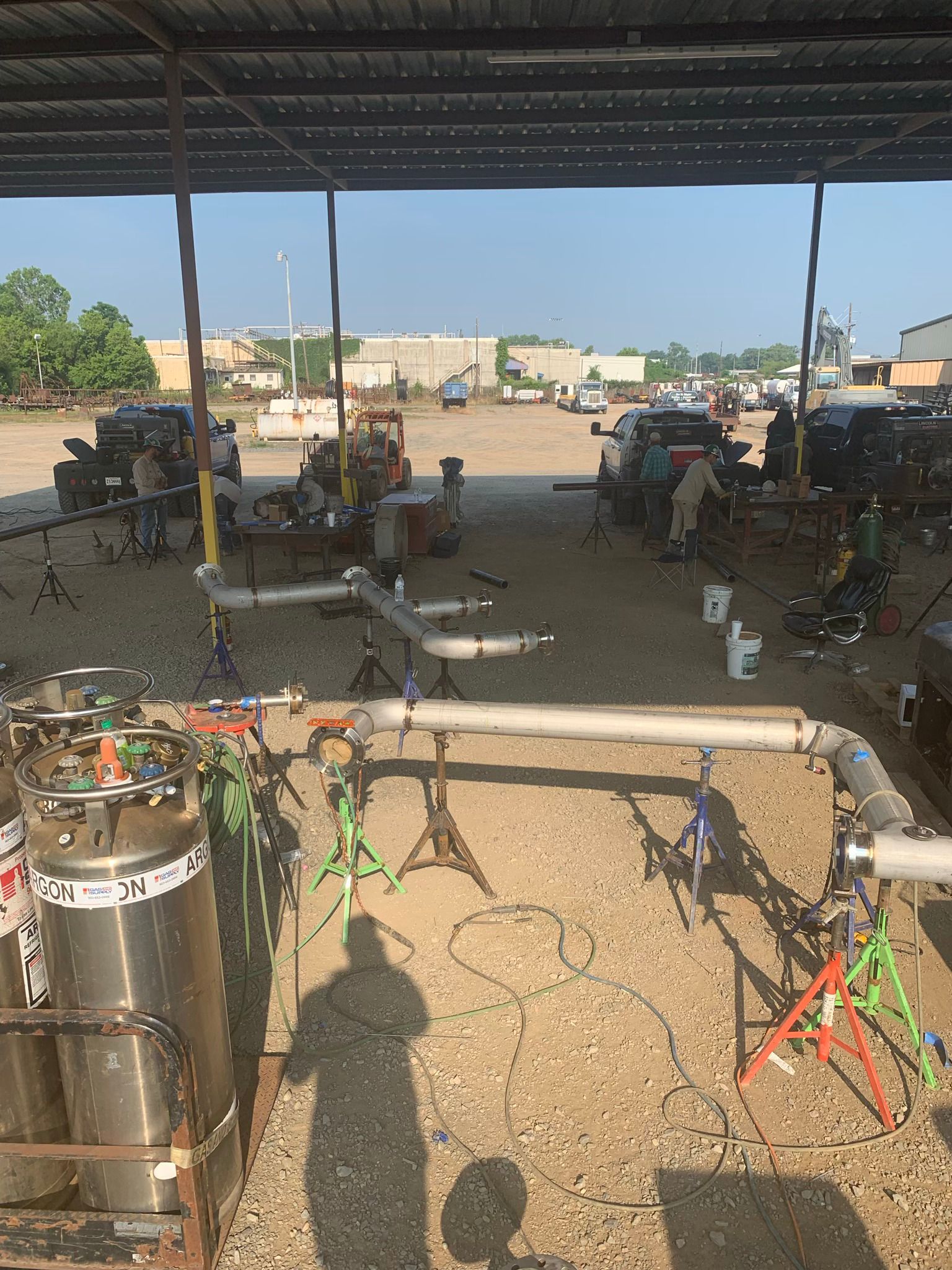 A bunch of pipes are sitting under a roof in a parking lot.