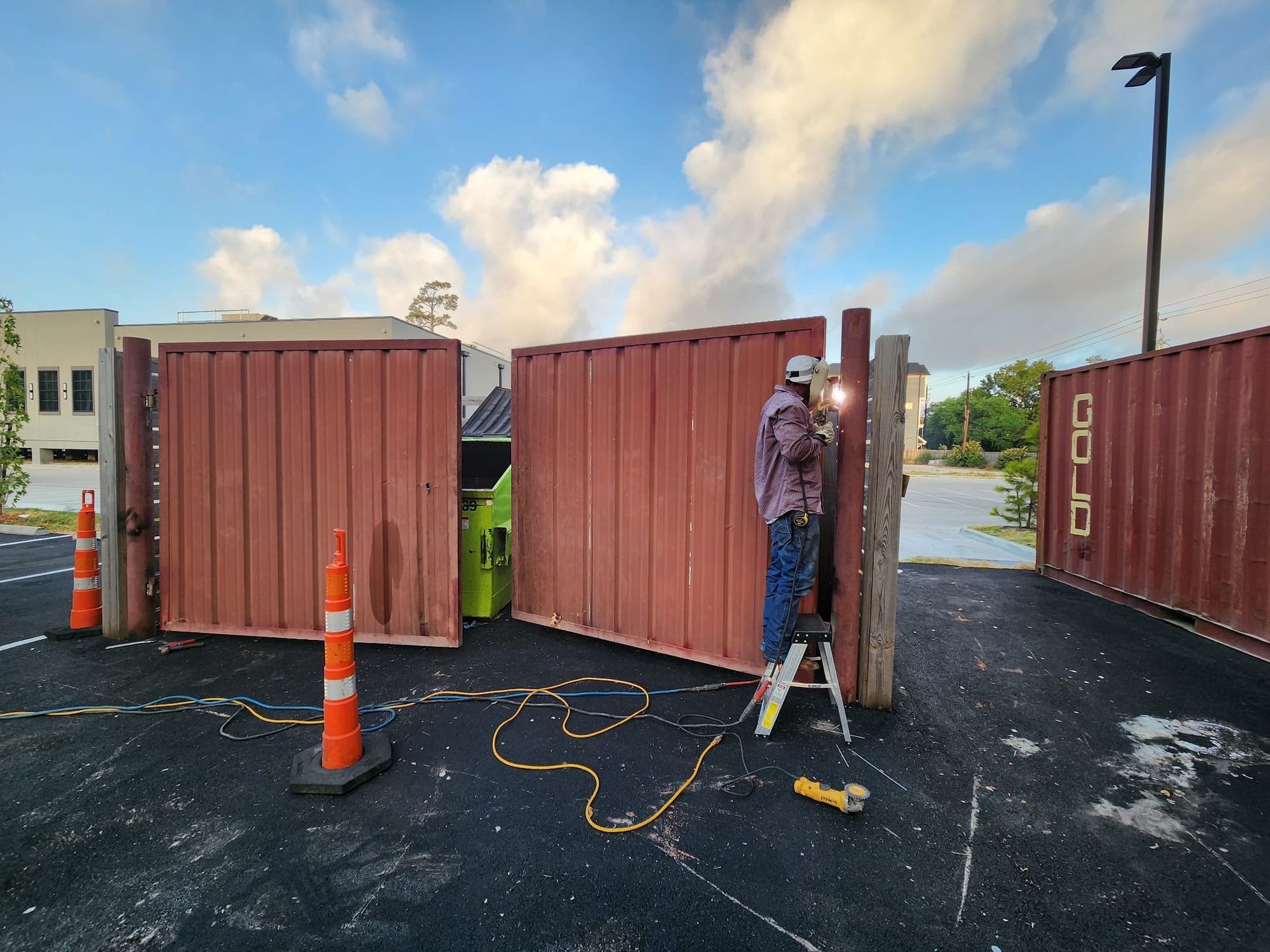 A man is welding a gate in a parking lot.