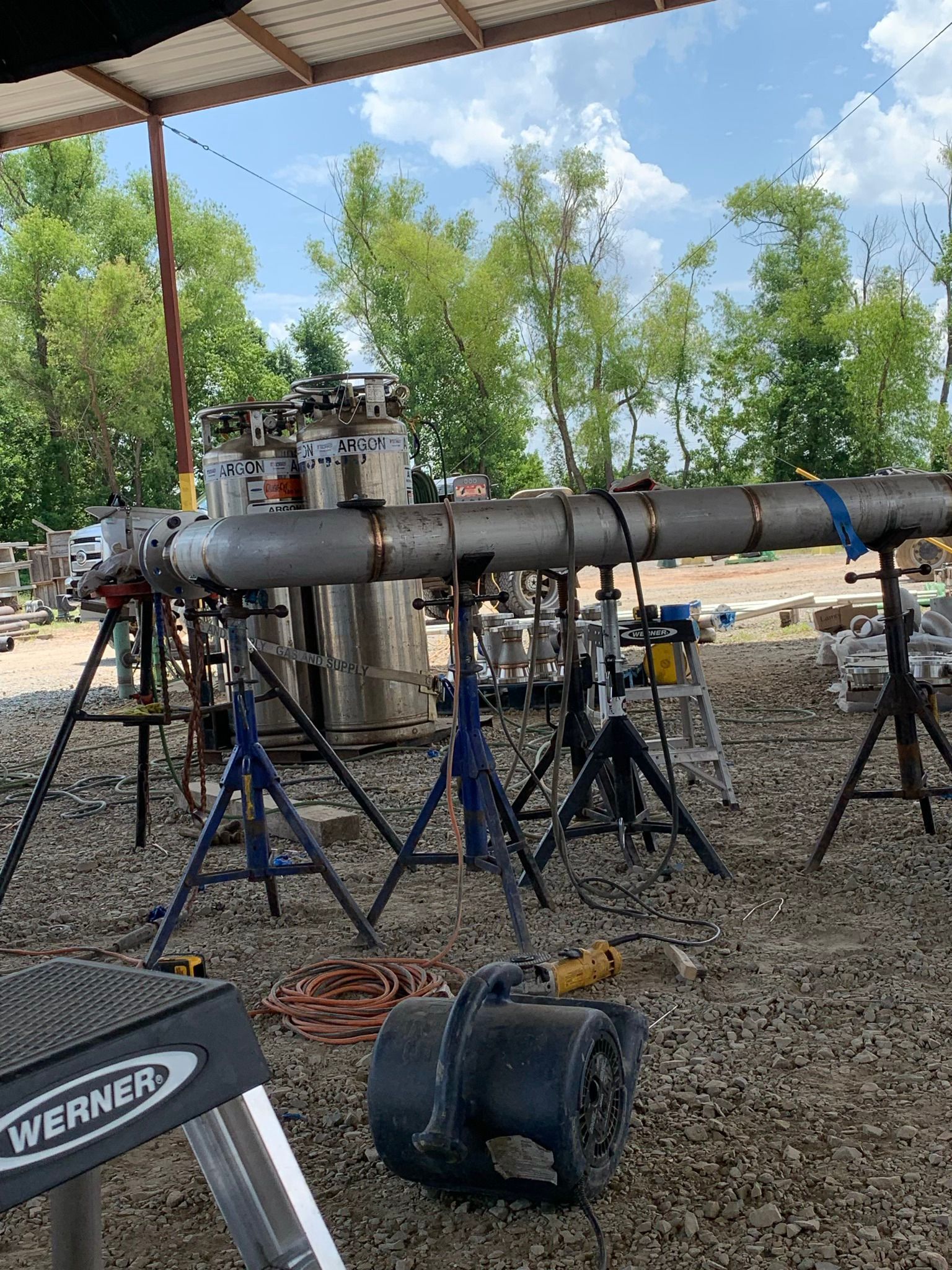 A large metal pipe is sitting on top of a pile of gravel under a canopy.