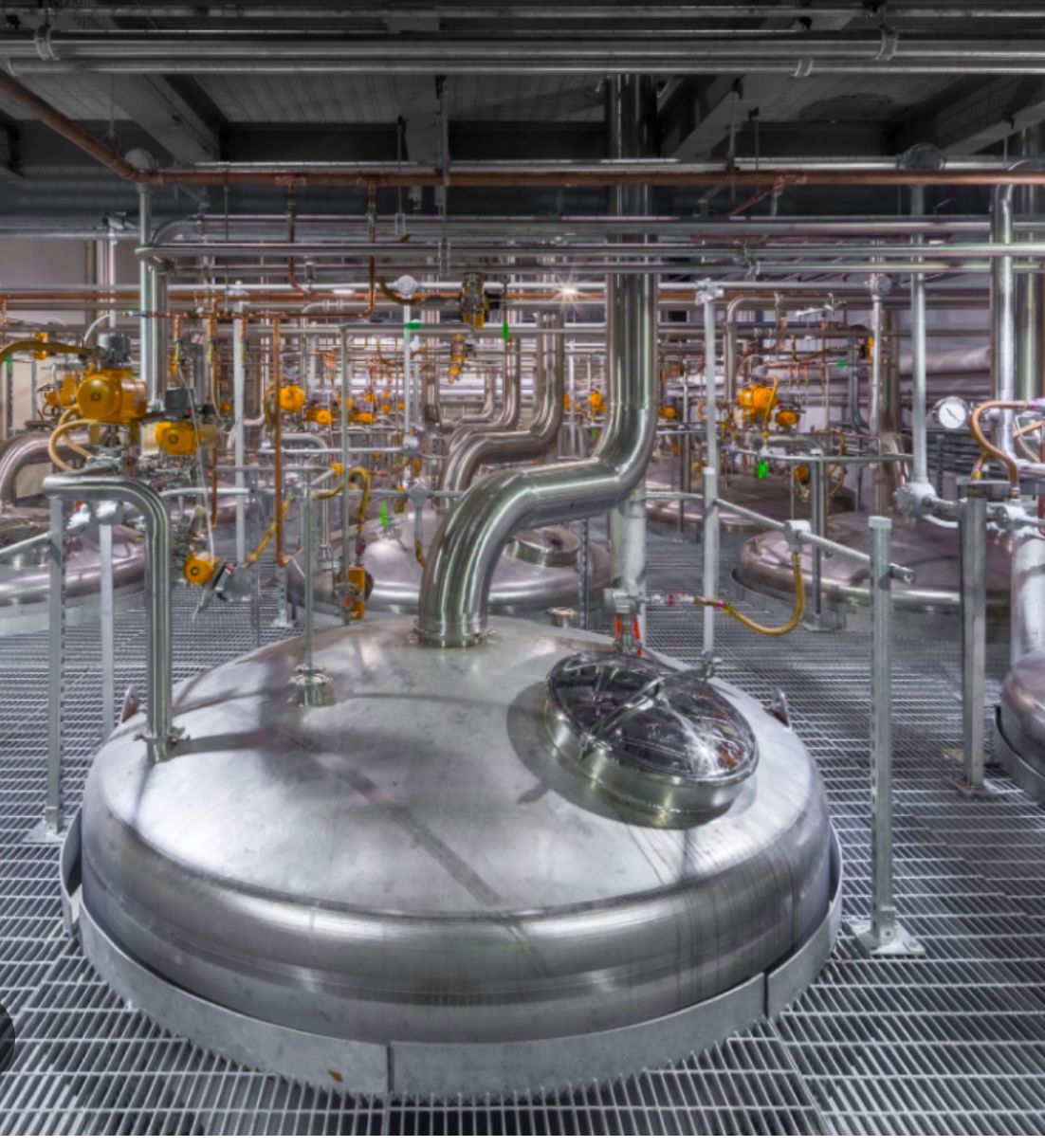A large stainless steel tank is surrounded by pipes in a factory.