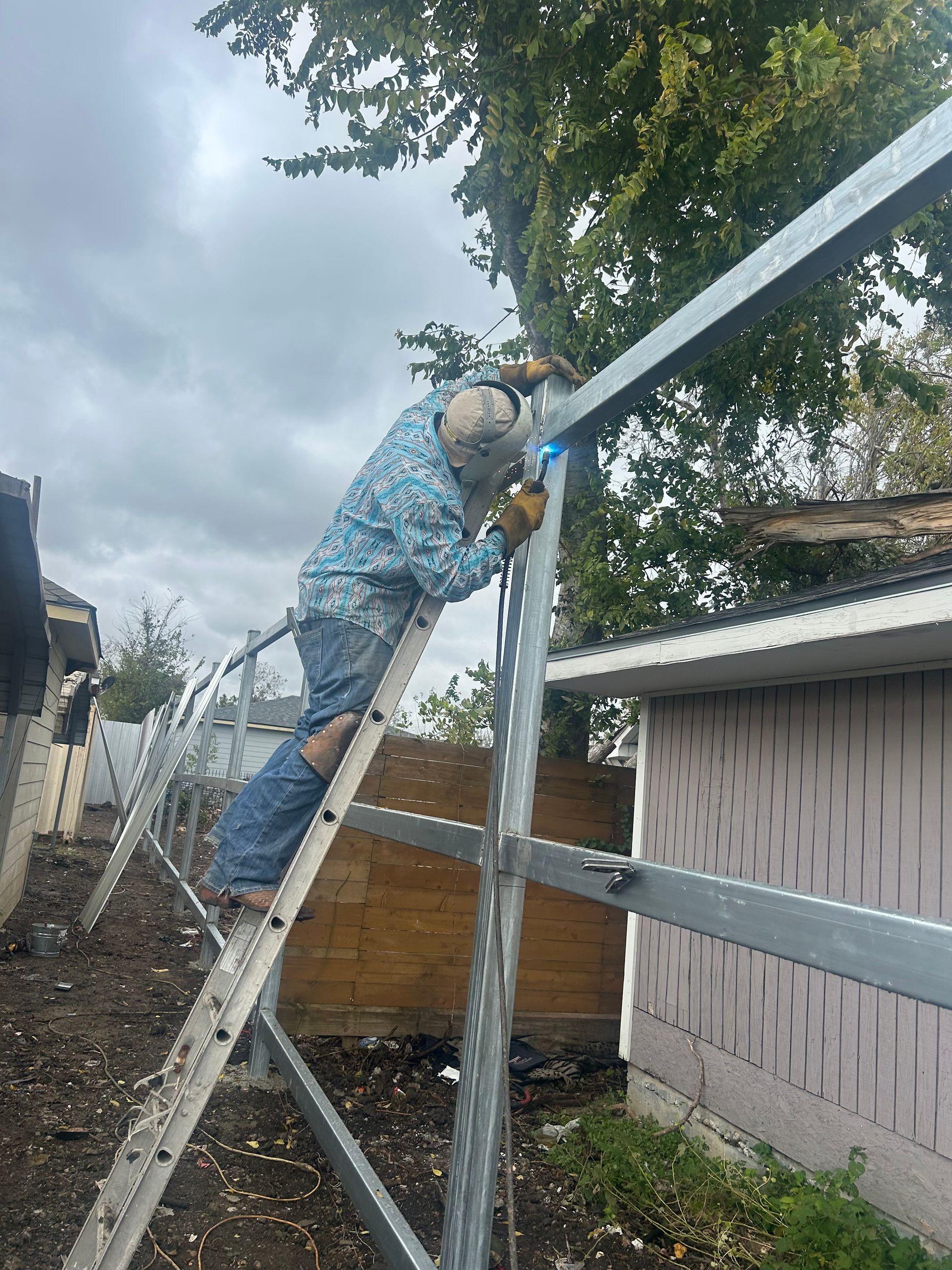 A man is standing on a ladder welding a metal structure.