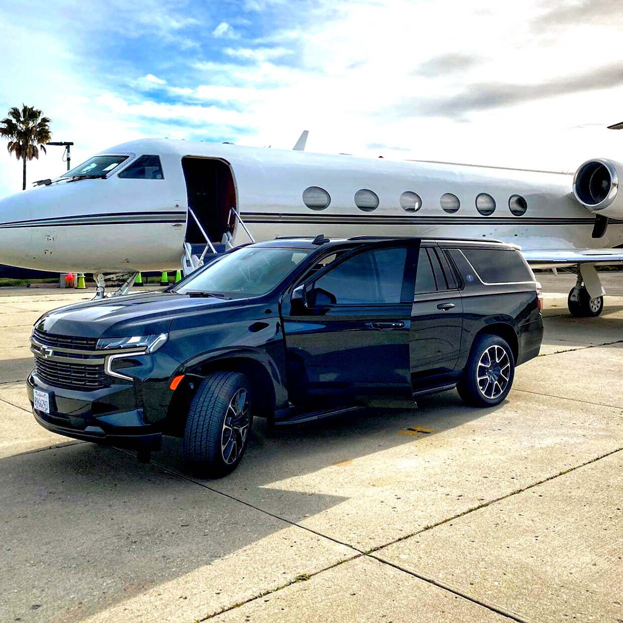 A black SUV parked next to a private jet on a tarmac; the SUV's doors are open.