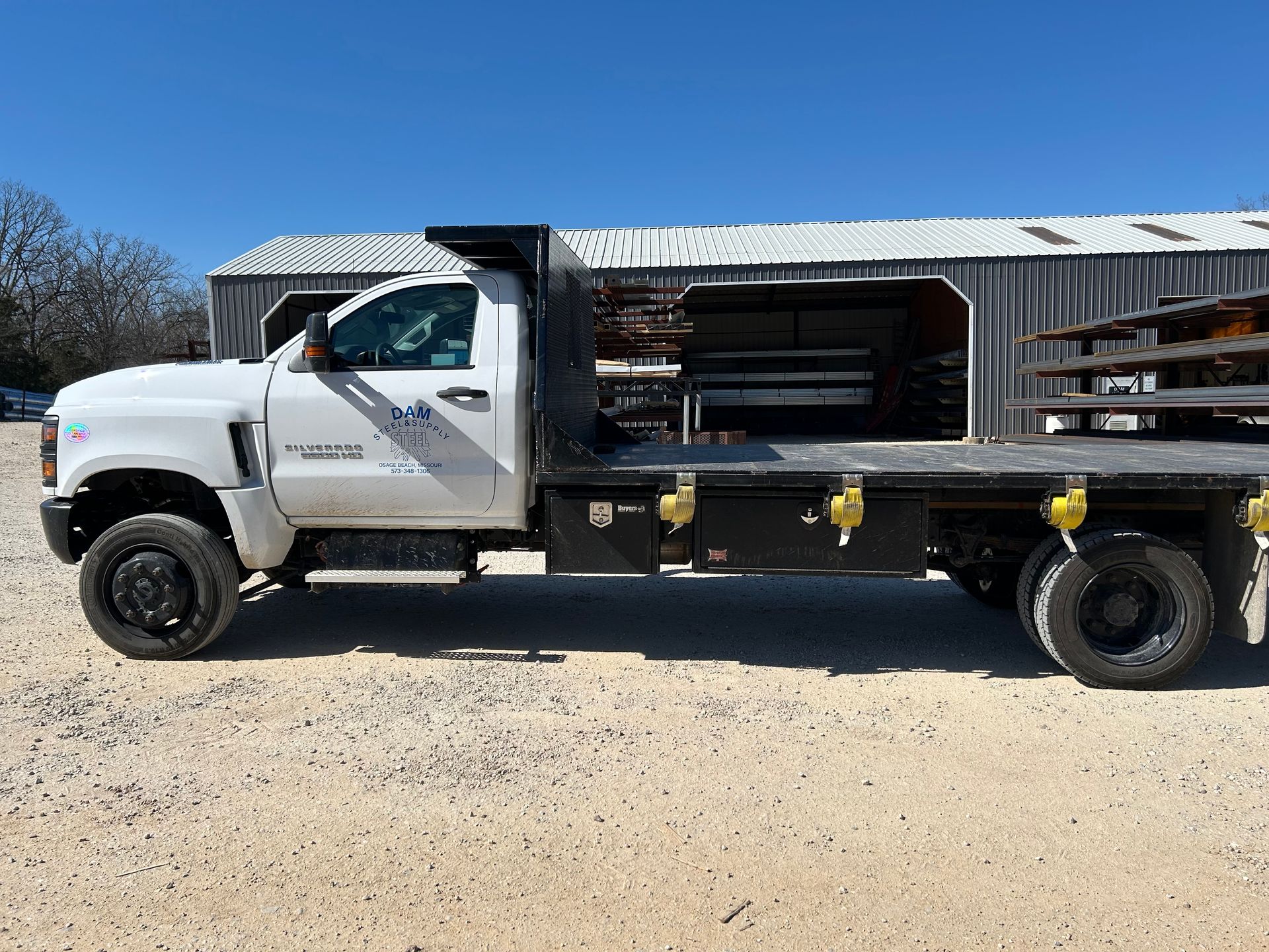 White flatbed service truck parked on a gravel lot under a clear sky