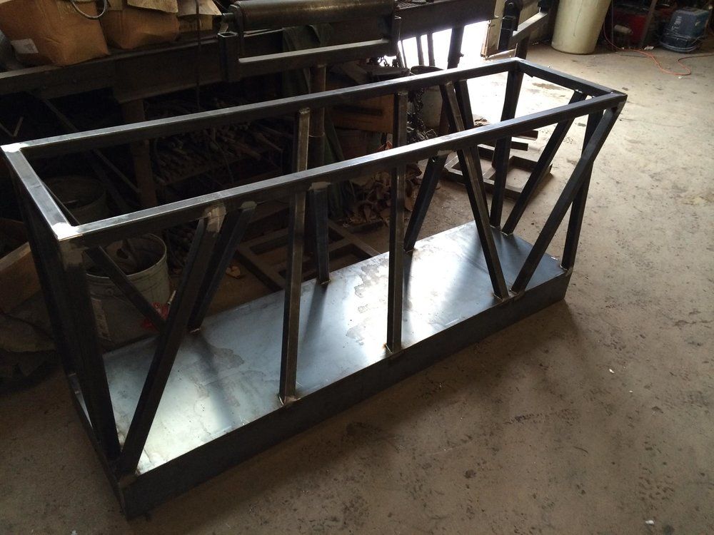 Black metal rectangular frame with diagonal supports, lying on a workshop floor.
