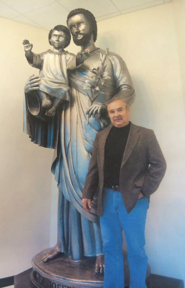 Person standing beside a large statue in a hallway, wearing a dark blazer and blue jeans.